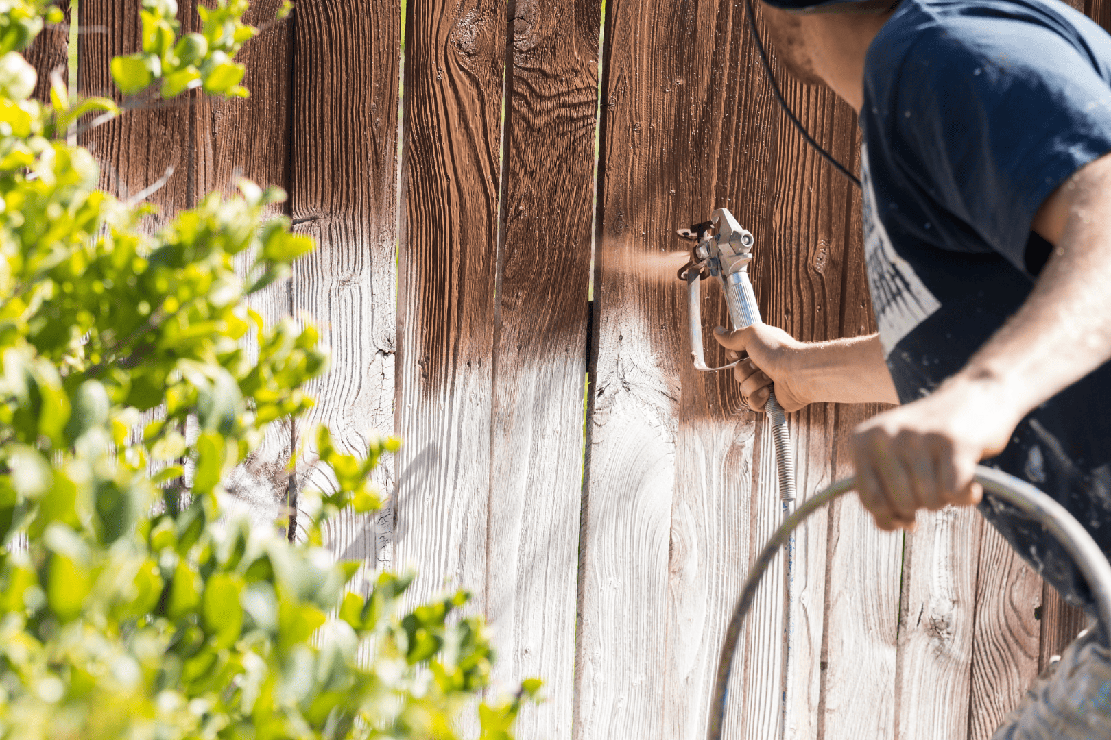 A man applying sealant to a wood fence to protect it from harsh weather conditions.
